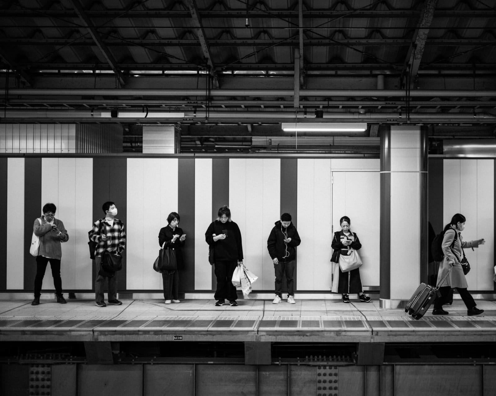 Commuters on urban Tokyo train station platform using smartphones and waiting.