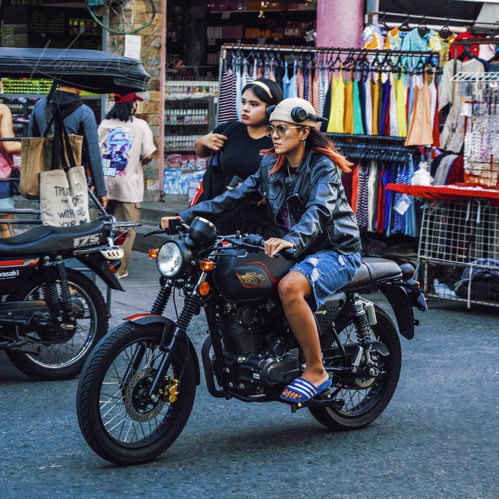 Young woman rides motorcycle through colorful urban Philippines market.