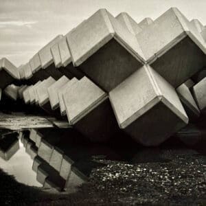 Brutalist photography of concrete breakwater blocks in a diagonal row at Ena port, Iwaki, mirrored in a puddle